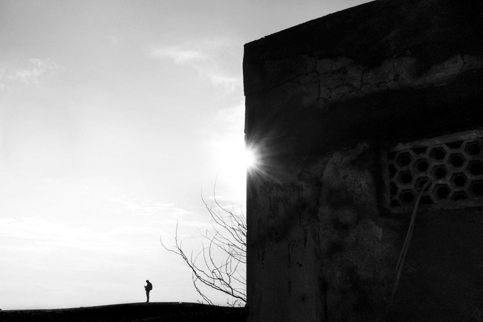 Black-and-white: a tiny figure on a ridge beside a sunlit wall
