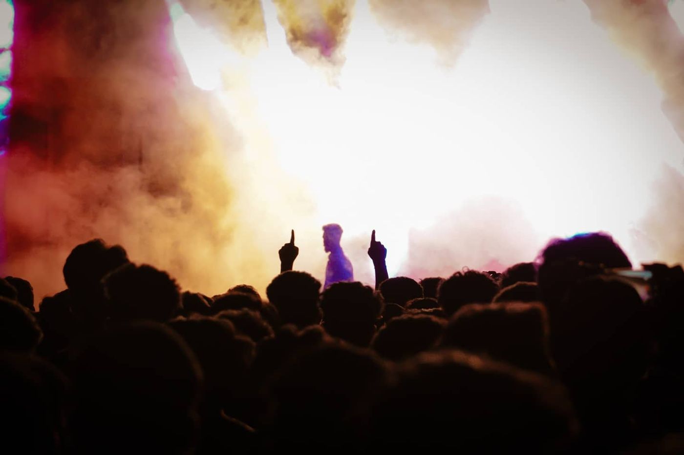 Silhouetted crowd at a concert, two fingers raised toward a hazy stage