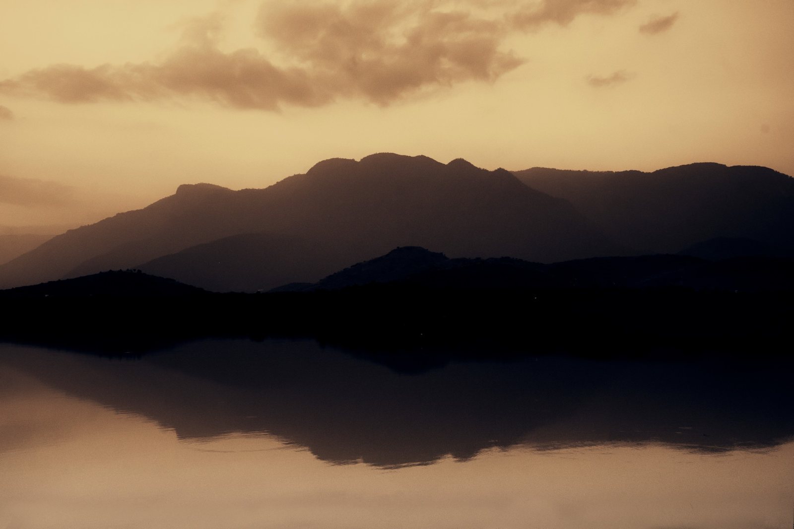 Mountains reflected in still water under a warm sky