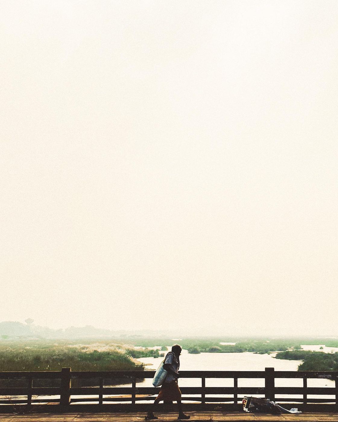 A man with a bag walking across a bridge in hazy morning light