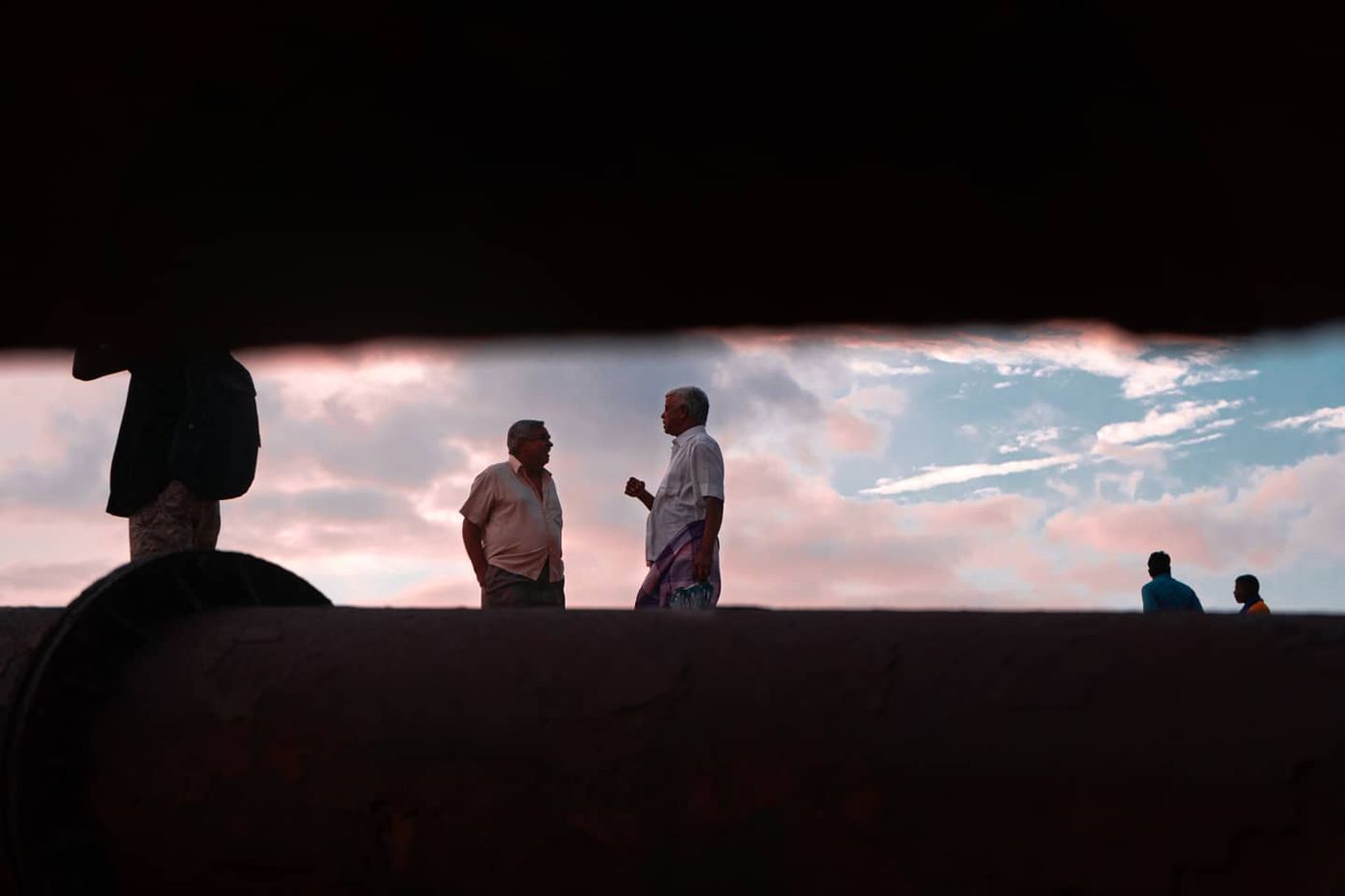 Two men talking against a pink sky, framed through a dark gap